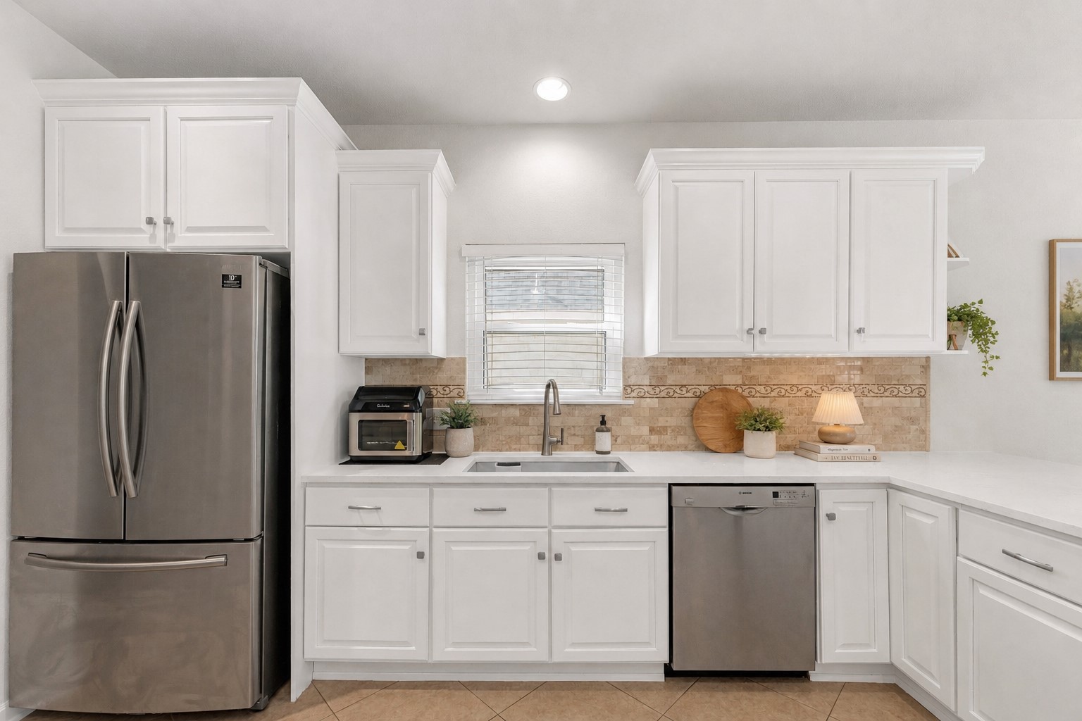 12528 Labrador Cove Austin, TX 78729 - Photo 15 of 40 Virtually Staged | Kitchen | Bright and inviting kitchen showcasing crisp white cabinetry, stainless steel appliances, extensive counter space, and elegant tile backsplash details. Thoughtfully enhanced with soft Pottery Barn-inspired décor, natural wood accents, fresh greenery, and warm neutral tones to highlight the kitchen’s spacious layout, abundant storage, and timeless design. A beautiful blend of style and functionality, perfect for everyday living and entertaining. Virtual staging is for illustrative purposes only.