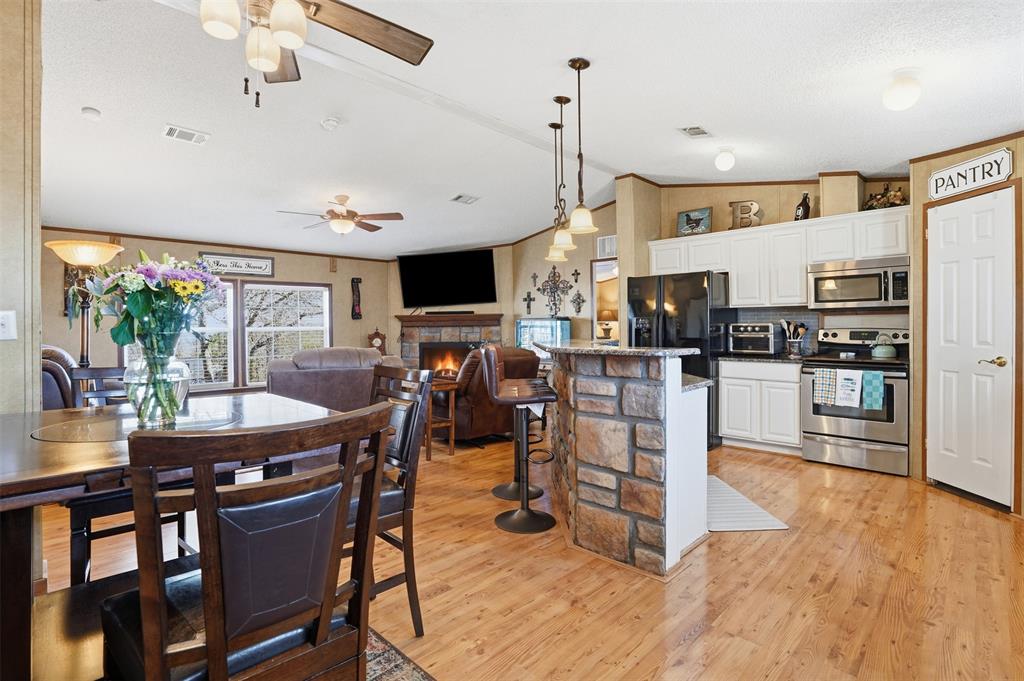 224 Cactus Ridge Court Springtown, TX 76082 - Photo 14 of 39 Kitchen featuring white cabinetry, decorative light fixtures, stainless steel appliances, a lit fireplace, and vaulted ceiling