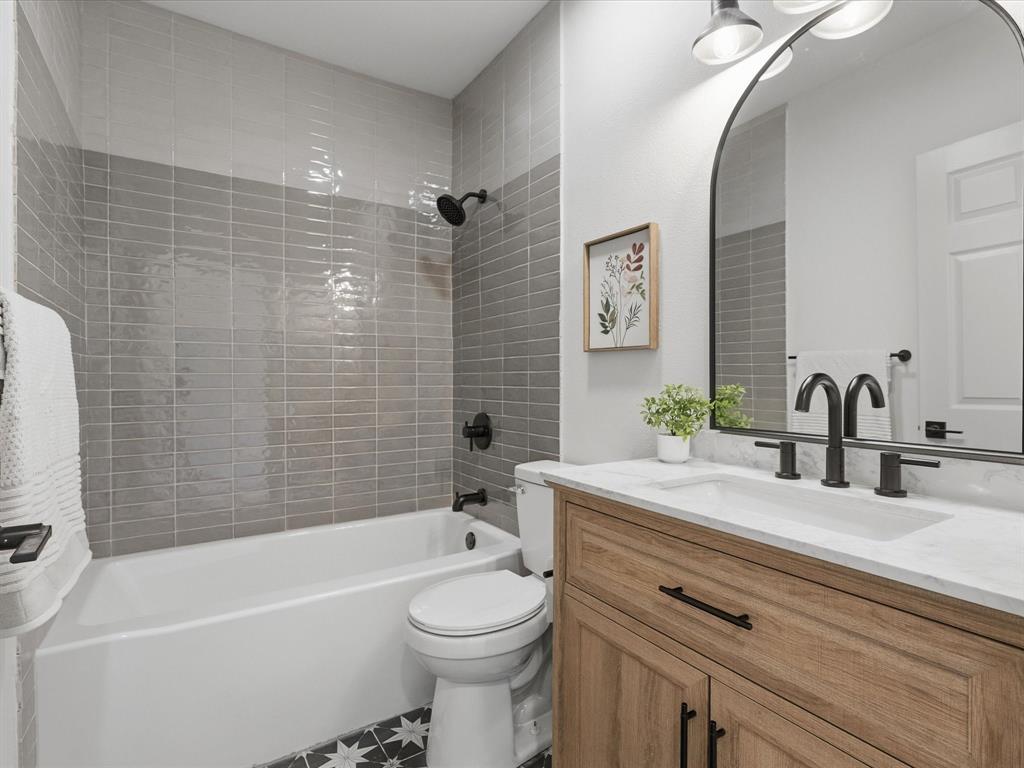 289 County Road 4655 Rhome, TX 76078 - Photo 14 of 34 Second Bathroom featuring a wood-finish vanity with a white countertop and integrated sink, a deep soaking tub with subway tile surround, a black arched mirror, and contrasting patterned floor tiles