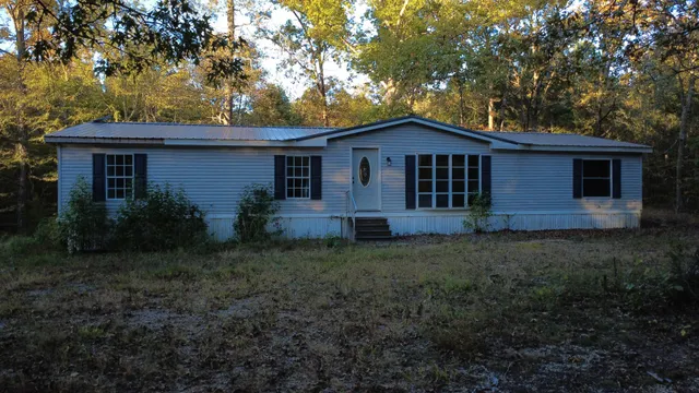 a view of a wooden house with large trees and a yard