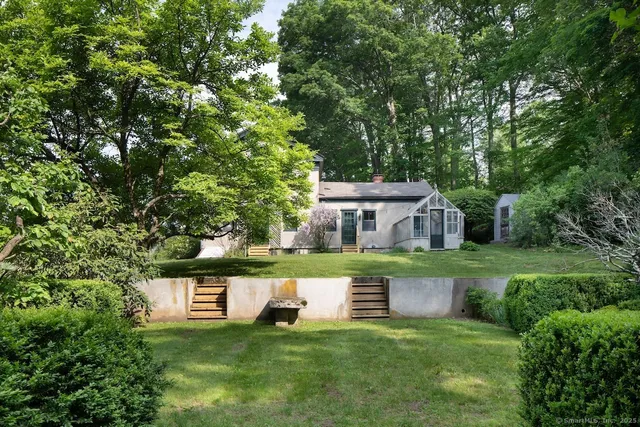 a view of a white house with a small yard and a large tree