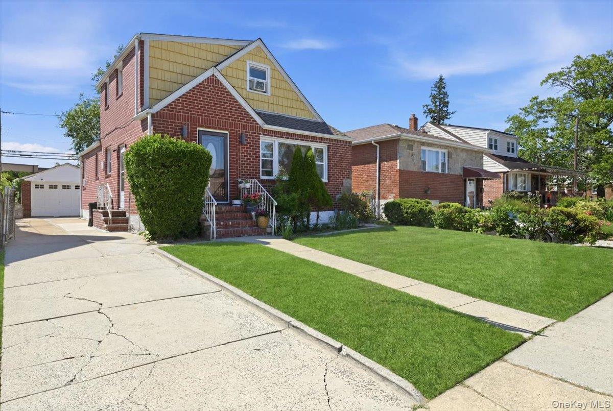 79 Wellington Road Elmont, NY 11003 - Photo 2 of 33 Brick and siding exterior residence featuring a front lawn and a long concrete driveway leading to a detached garage