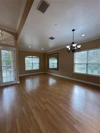 an empty room with wooden floor chandelier and windows