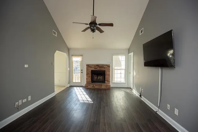 a view of a livingroom with a fireplace a ceiling fan and windows