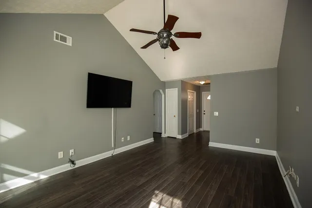 a view of an empty room with wooden floor and a ceiling fan