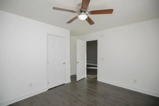 an empty room with wooden floor ceiling fan and window