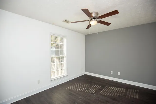 a view of an empty room with wooden floor and a ceiling fan