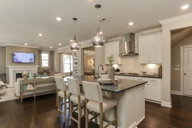 a kitchen with stainless steel appliances kitchen island granite countertop a stove a sink a refrigerator white cabinets and couches with wooden floor