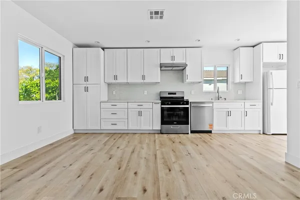 a kitchen with stainless steel appliances granite countertop a stove top oven a sink dishwasher and a refrigerator with wooden floor