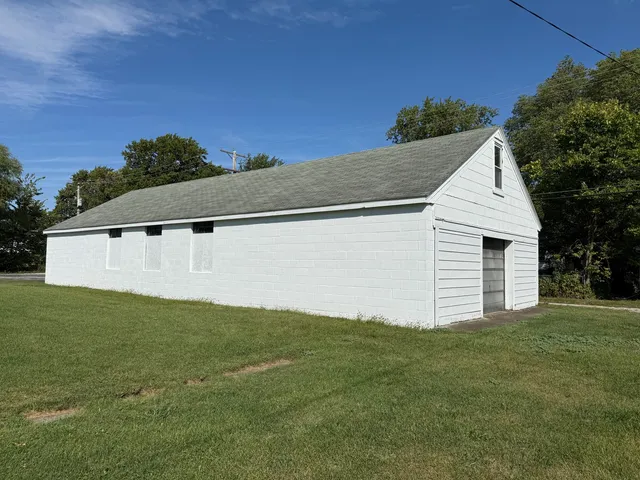 a backyard of a white house with plants and large tree