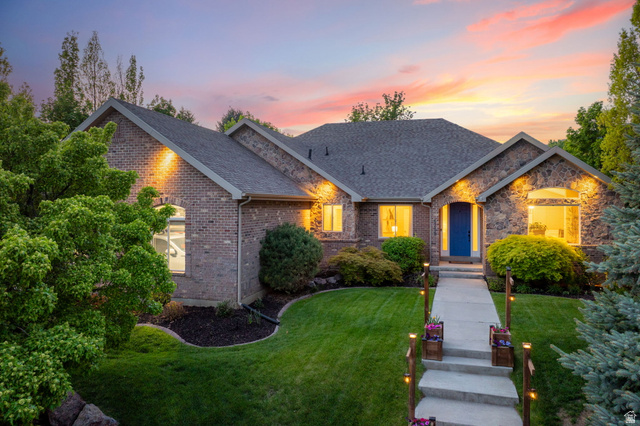 6208 West Bull River Road Highland, UT 84003 - Photo 1 of 90 Brick and stone exterior featuring a blue entry door, gabled rooflines, a manicured lawn, and a concrete walkway with integrated lighting