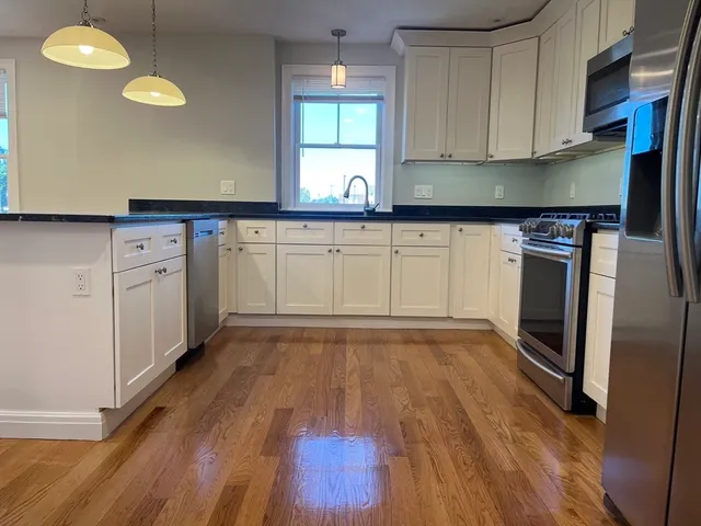 a kitchen with granite countertop a stove a sink and white cabinets with wooden floor