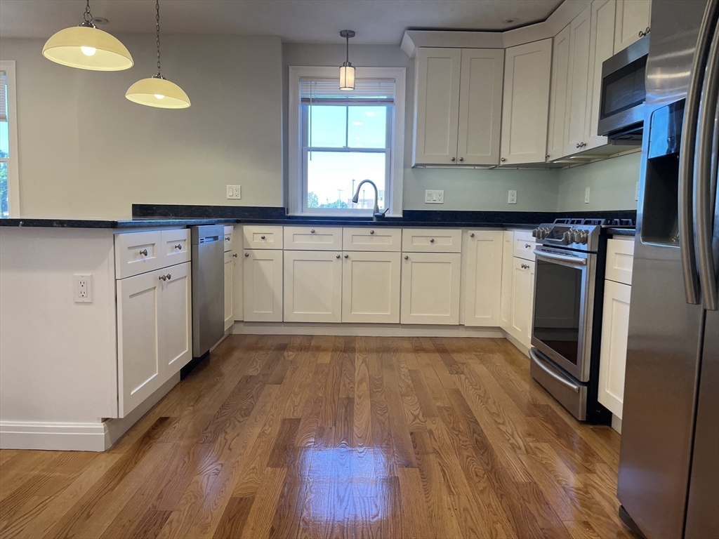 a kitchen with granite countertop a stove a sink and white cabinets with wooden floor