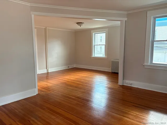 an empty room with wooden floor and windows with curtains