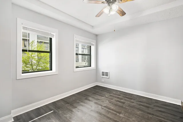 an empty room with wooden floor chandelier fan and windows