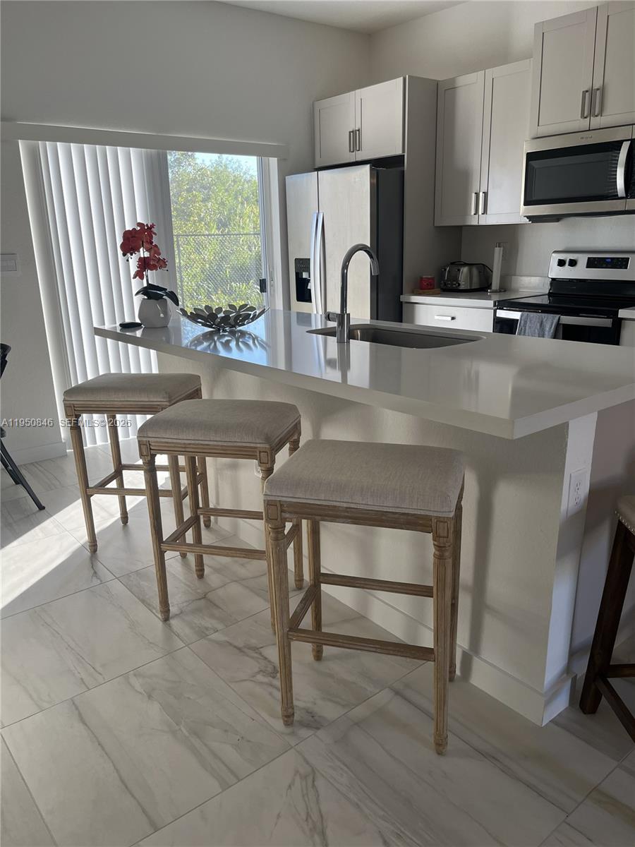 784 Southeast 19th Street, Unit 784 Homestead, FL 33034 - Photo 5 of 22 a kitchen with stainless steel appliances a table chairs microwave and sink