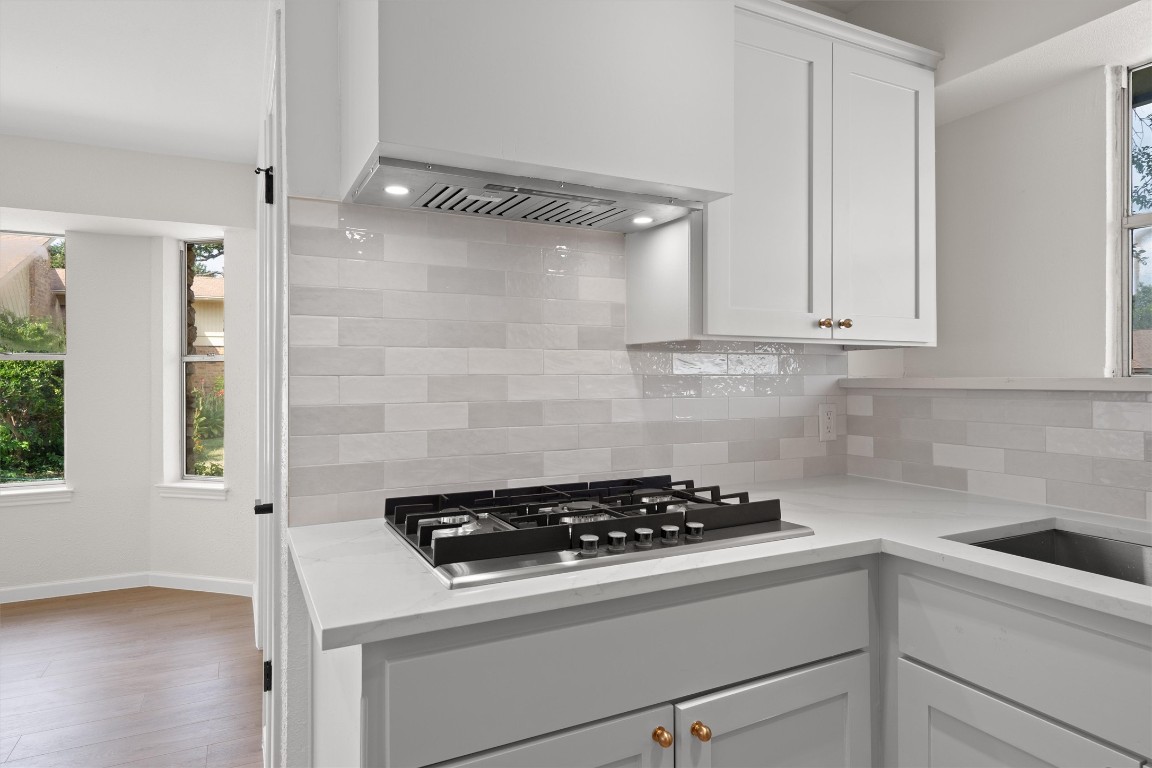 7008 Beckett Road Austin, TX 78749 - Photo 10 of 23 Kitchen with white cabinets, backsplash, stainless steel gas stovetop, premium range hood, and light stone counters