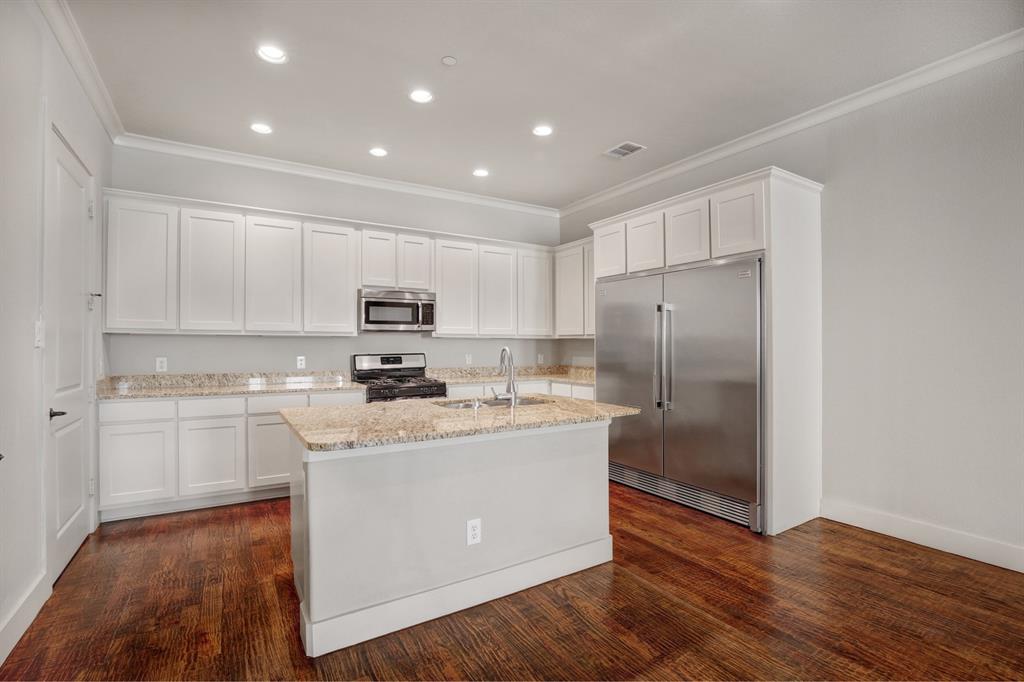 4111 Rawlins Street, Unit 403 Dallas, TX 75219 - Photo 9 of 23 Kitchen featuring white shaker cabinetry, speckled countertops, stainless steel appliances, a central island, and wood-finish flooring