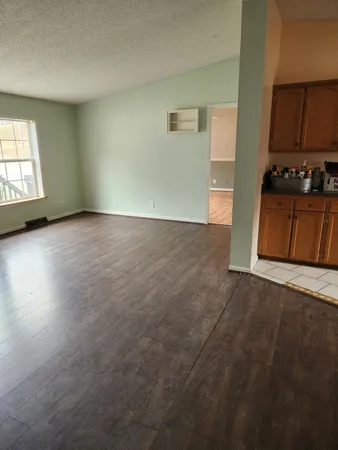an empty room with wooden floor and kitchen view