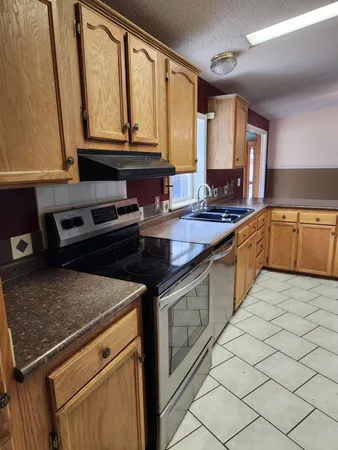 a kitchen with granite countertop a sink a stove top oven and cabinetry