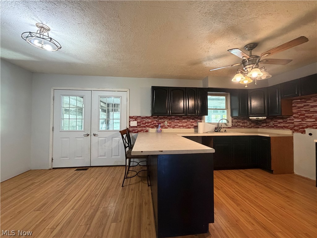3950 Wolf Road Southwest Port Washington, OH 43837 - Photo 11 of 45 Wood-finish flooring, dark wood cabinetry, light-toned countertops, red tile backsplash, and a ceiling fan with integrated lighting