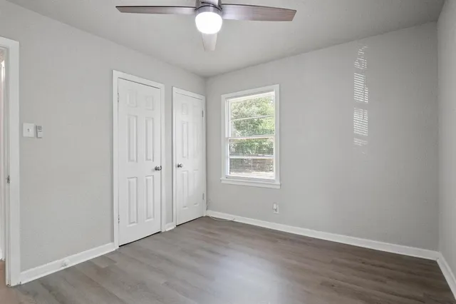an empty room with wooden floor fan and windows