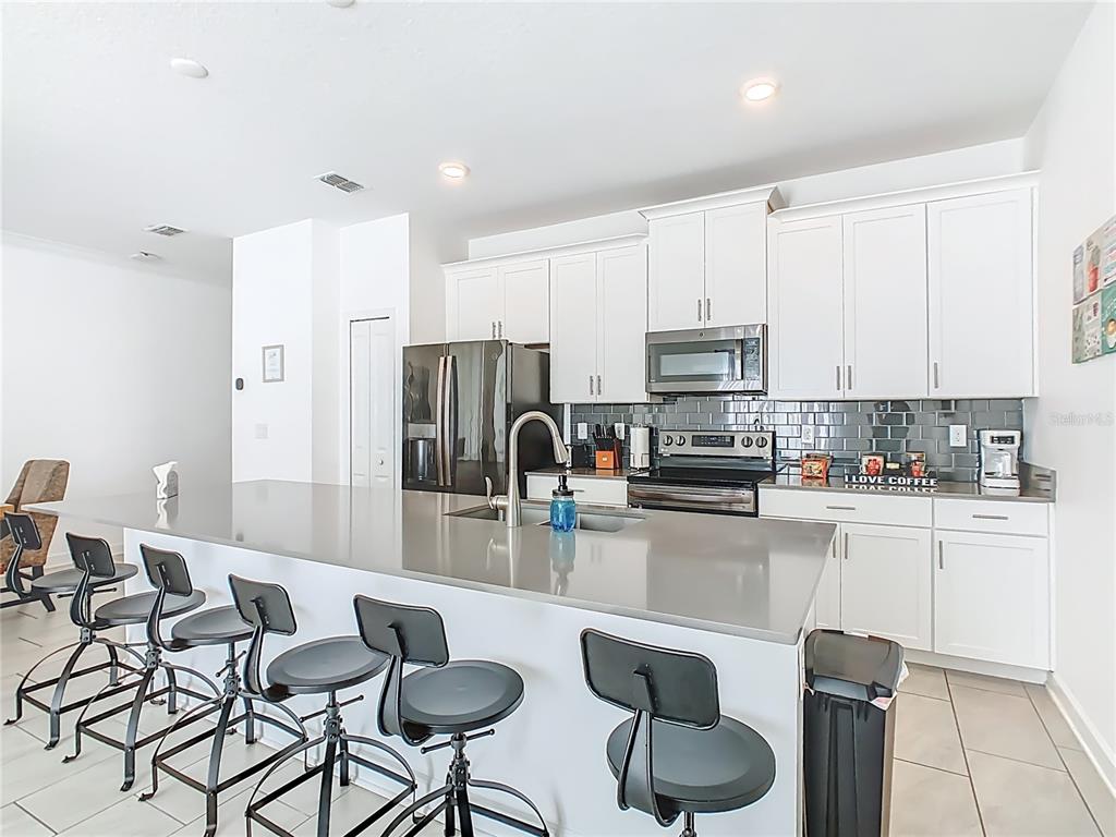 2957 Simile Street Kissimmee, FL 34746 - Photo 10 of 67 a kitchen with stainless steel appliances granite countertop a stove top oven a refrigerator a sink and a dining table with white cabinets