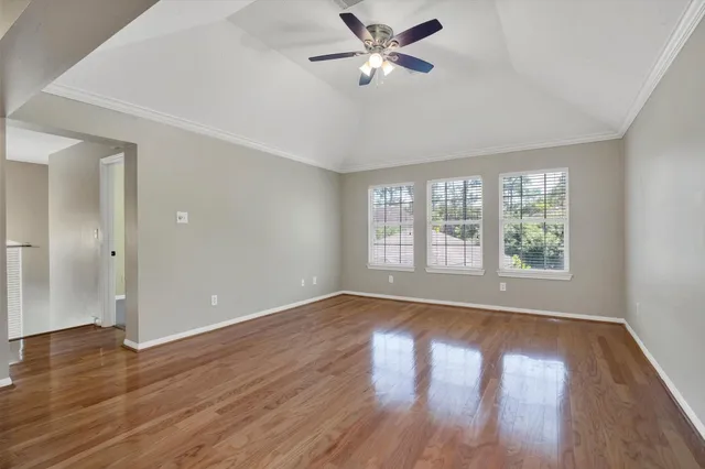 an empty room with wooden floor fan and windows
