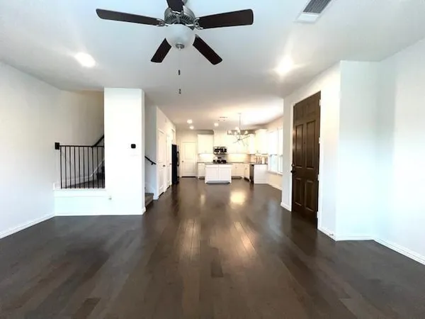 a view of a hallway with wooden floor a ceiling fan and kitchen view