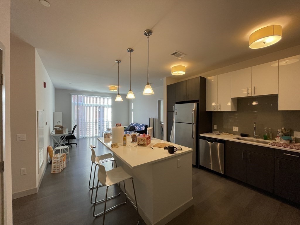 99 Tremont Street, Unit 313 Boston, MA 02135 - Photo 2 of 13 a kitchen with stainless steel appliances kitchen island granite countertop a sink a stove a refrigerator and island with wooden floor