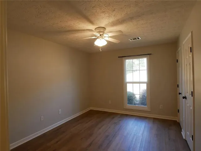 an empty room with wooden floor fan and windows