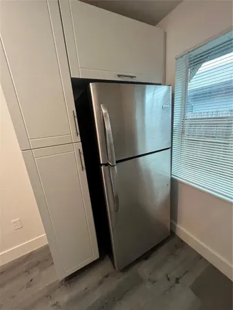 a view of a refrigerator in kitchen and an empty room with wooden floor