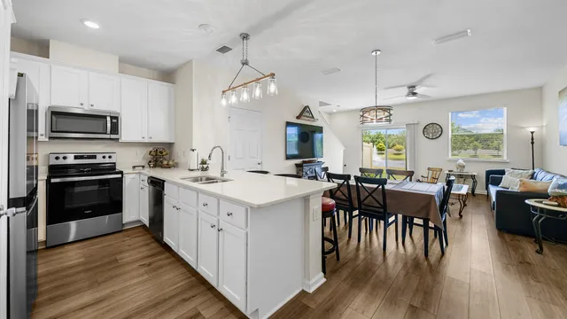 a open kitchen with stainless steel appliances granite countertop a stove a refrigerator a kitchen island a stove and a dining table with wooden floor