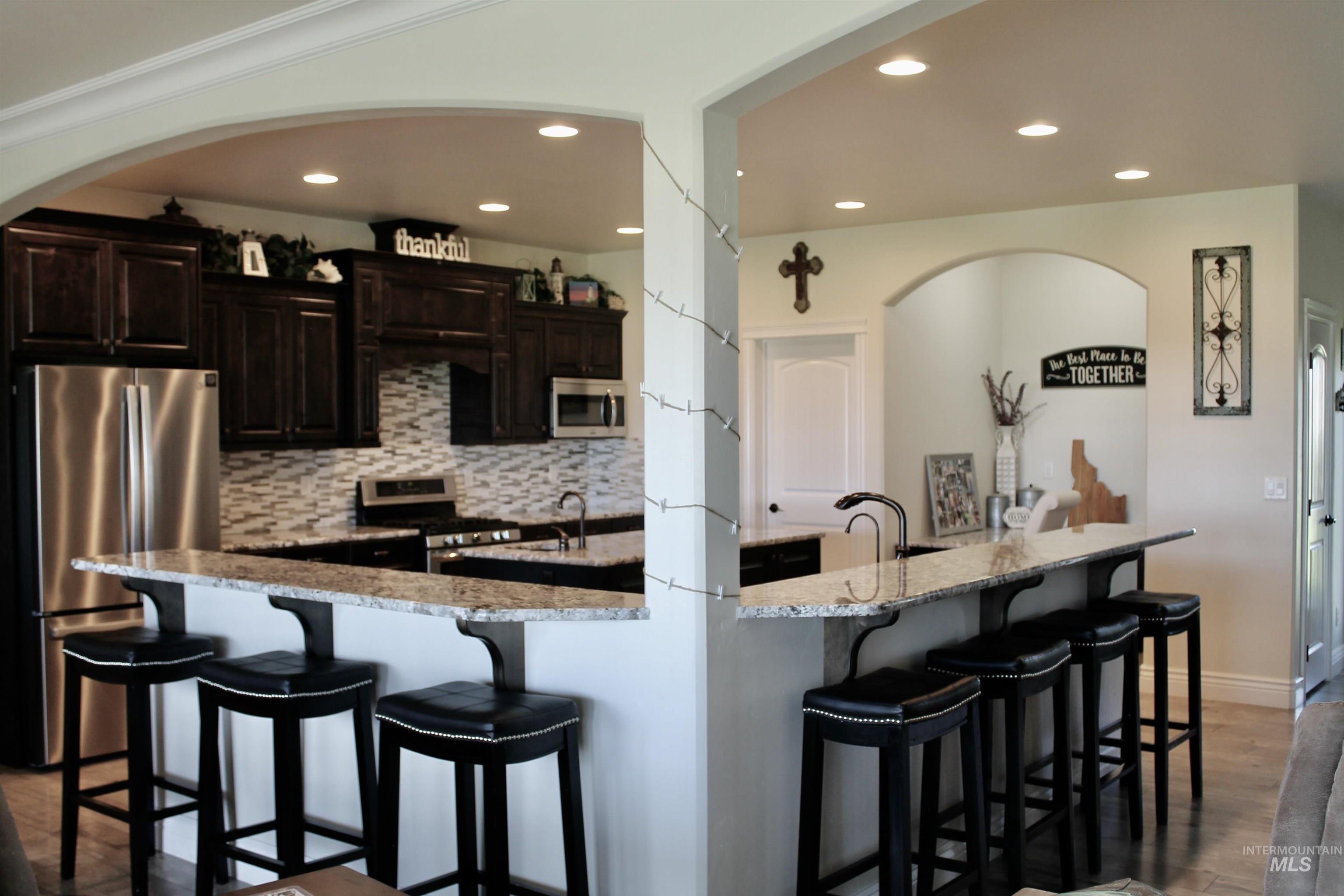 2464 Windmill Drive Twin Falls, ID 83301 - Photo 16 of 47 Kitchen featuring appliances with stainless steel finishes, recessed lighting, a kitchen bar, wood finished floors, and backsplash