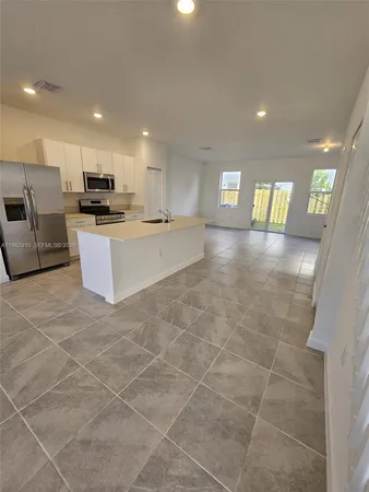 a view of a living room kitchen with stainless steel appliances a stove a sink a microwave and a refrigerator