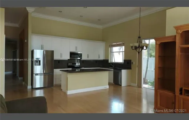 a kitchen with stainless steel appliances granite countertop a refrigerator a sink dishwasher a stove and a dining table with wooden floor