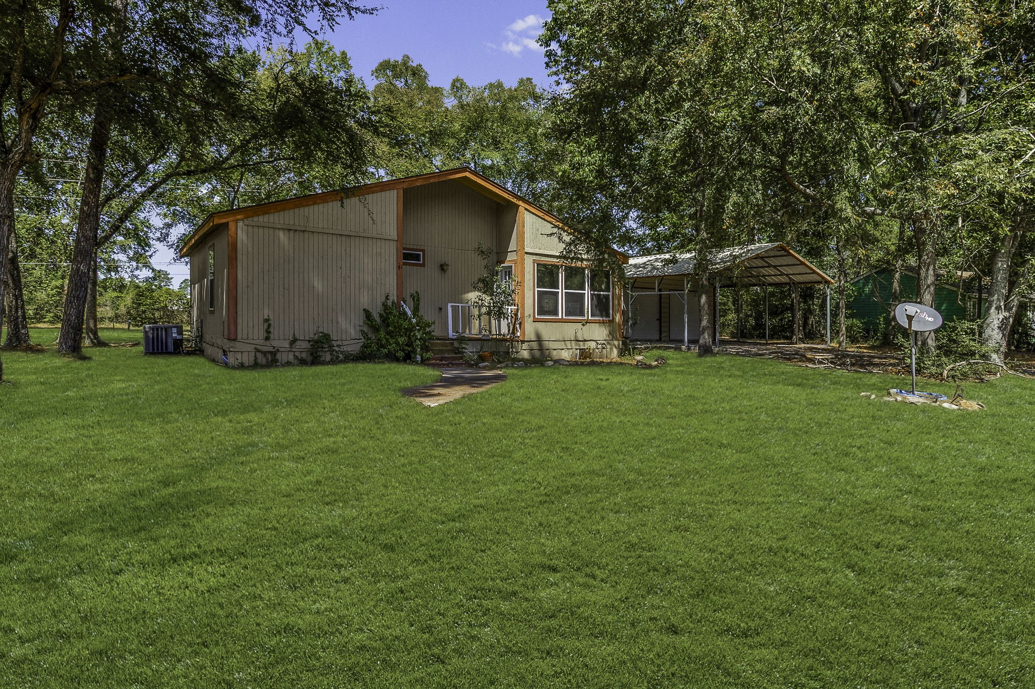 Charming single-story home nestled among mature trees, featuring a spacious lawn and a convenient carport.