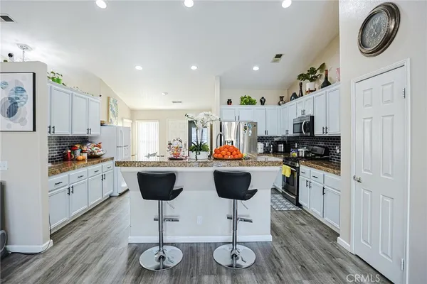 a kitchen with stainless steel appliances granite countertop a refrigerator a stove a sink dishwasher and white cabinets with wooden floor