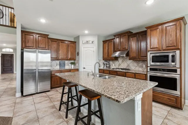 a kitchen with kitchen island granite countertop wooden cabinets a stove a oven and a refrigerator with wooden floor