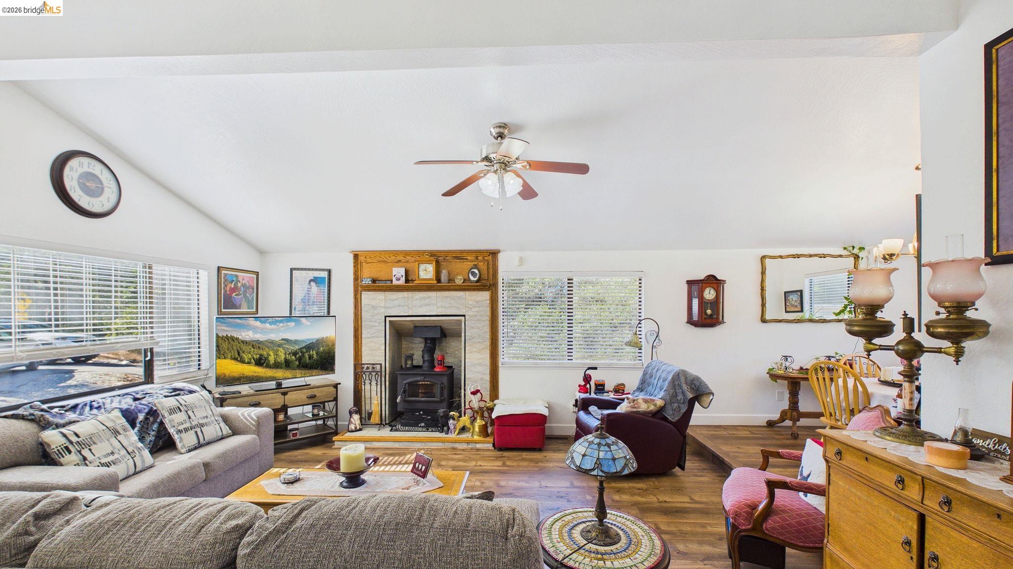 11858 Campo Seco Road Sonora, CA 95370 - Photo 10 of 45 Spacious living area featuring a vaulted ceiling with a ceiling fan, wood-finish flooring, a prominent fireplace with a wood-burning insert, and ample natural light from multiple windows