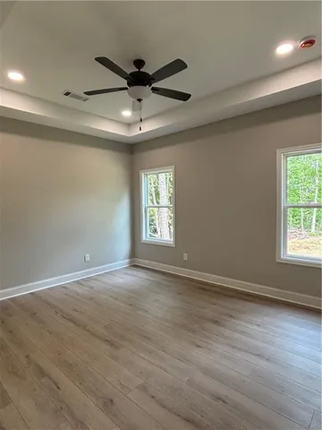 an empty room with wooden floor a ceiling fan and windows