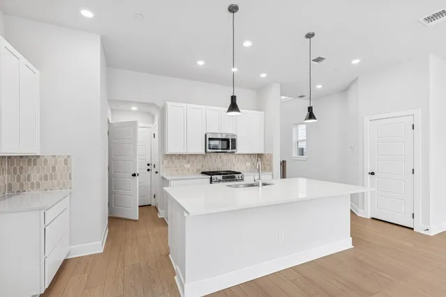 a large white kitchen with kitchen island a stove a sink a refrigerator and white cabinets with wooden floor