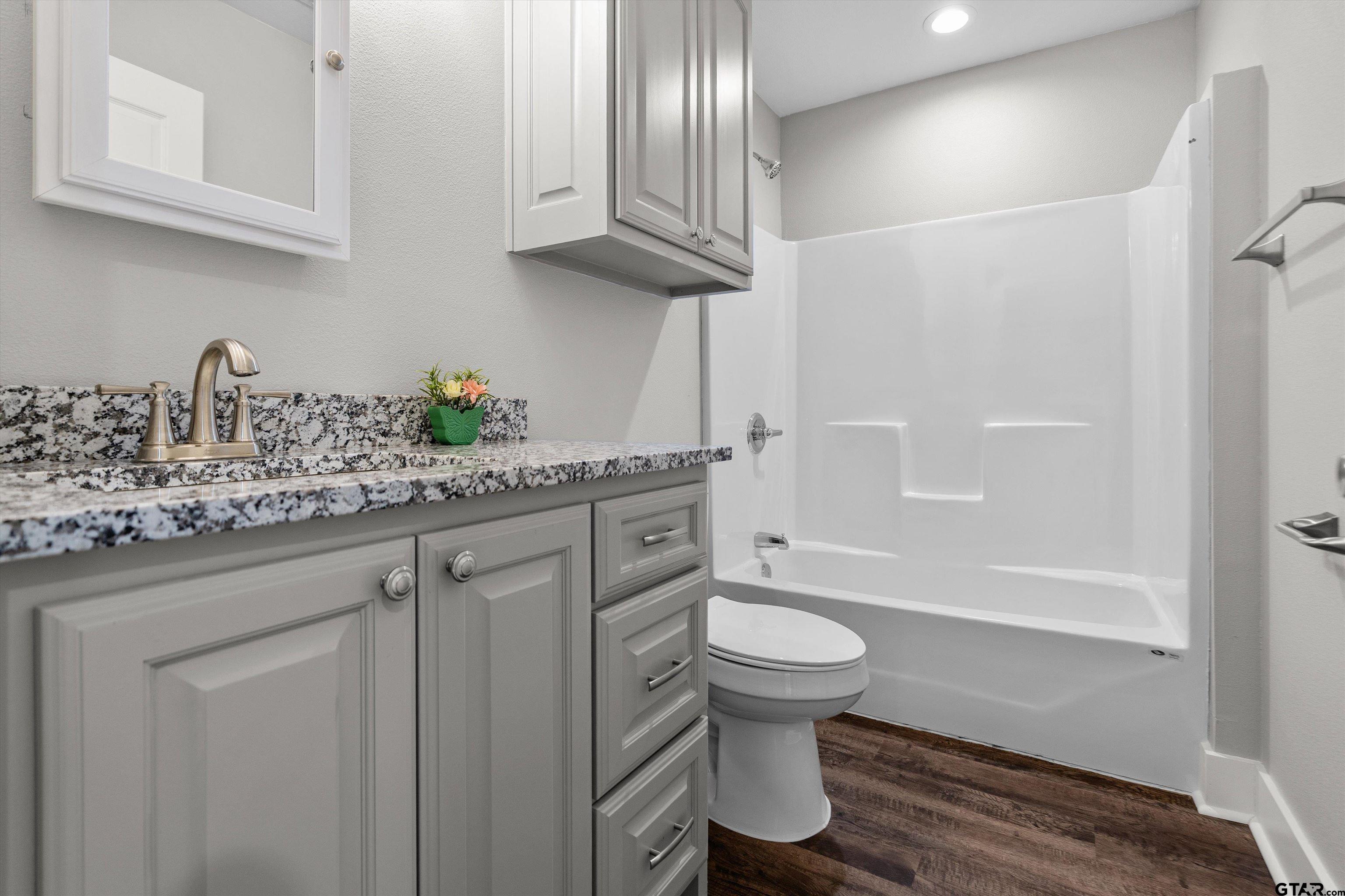 5881 Jefferson Avenue Tyler, TX 75708 - Photo 19 of 20 a bathroom with a granite countertop sink a toilet and bathtub