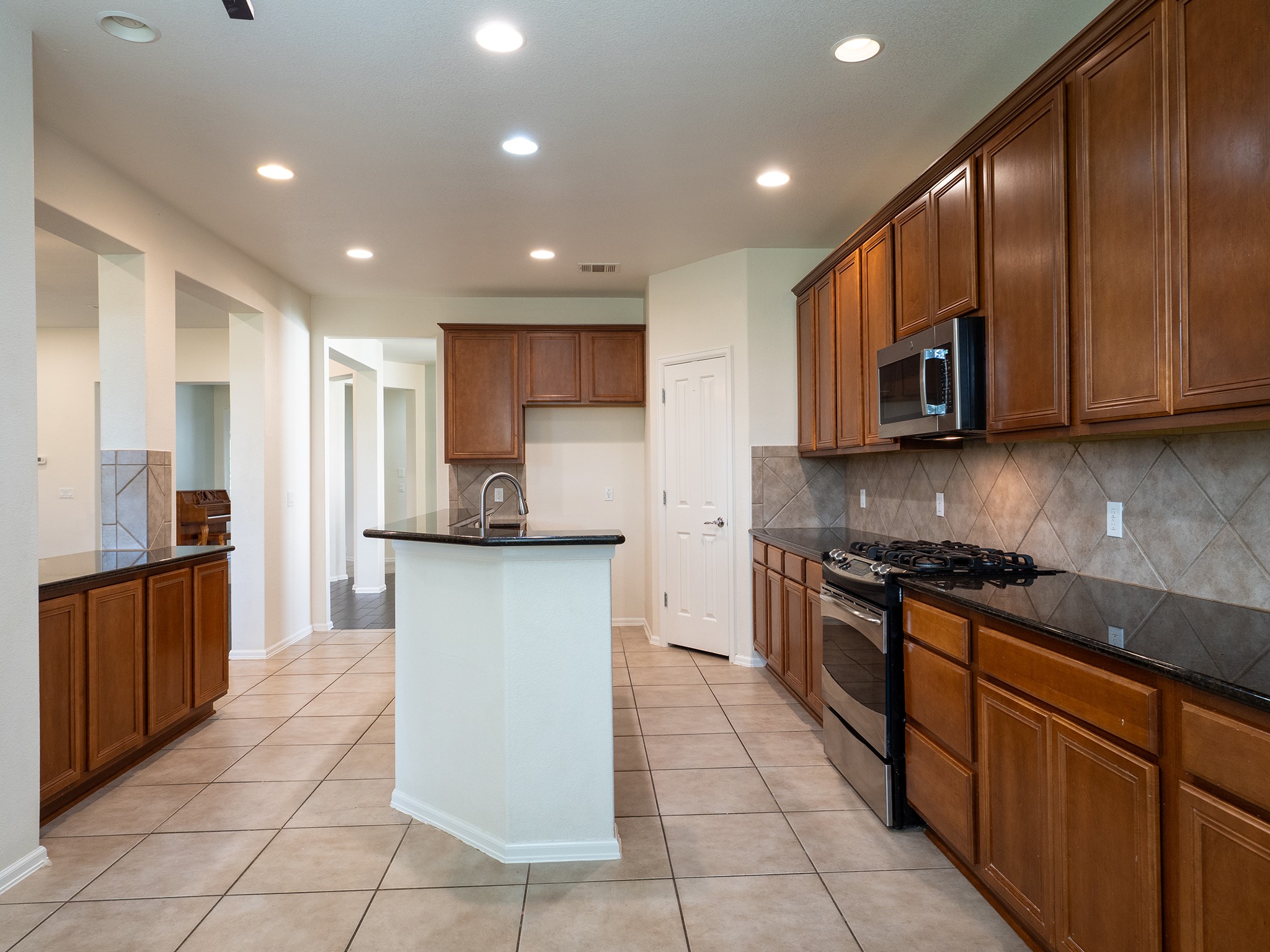 572 Big Meadow Road Austin, TX 78737 - Photo 7 of 32 A contemporary kitchen showcasing dark granite counters, warm wood cabinetry, and sleek stainless steel appliances.