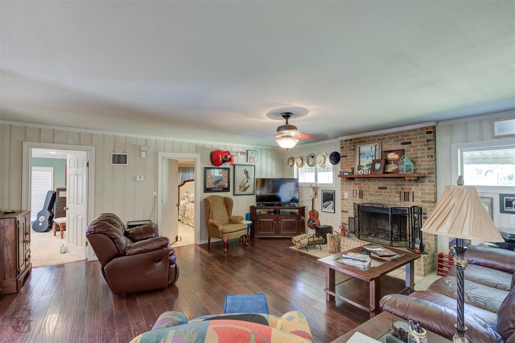 459 Dollie Moore Road Ringgold, LA 71068 - Photo 4 of 19 Hardwood-finish flooring, brick-faced fireplace with wood mantel, ceiling fan with light fixture, and multiple windows for natural light