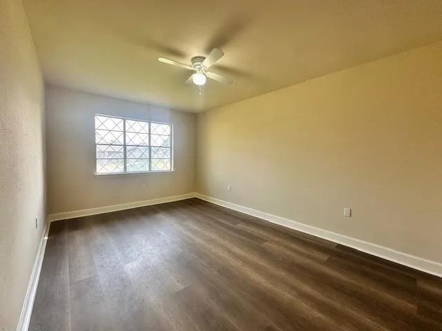 an empty room with wooden floor fan and windows