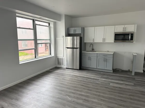 a view of kitchen with stainless steel appliances granite countertop a stove top oven a refrigerator and white cabinets with wooden floor