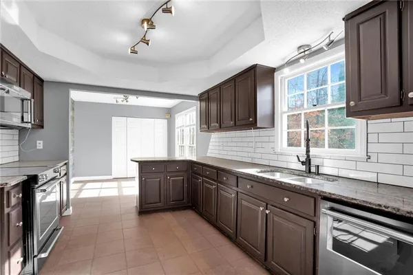 a large kitchen with granite countertop a sink and dishwasher a oven a stove with wooden cabinets