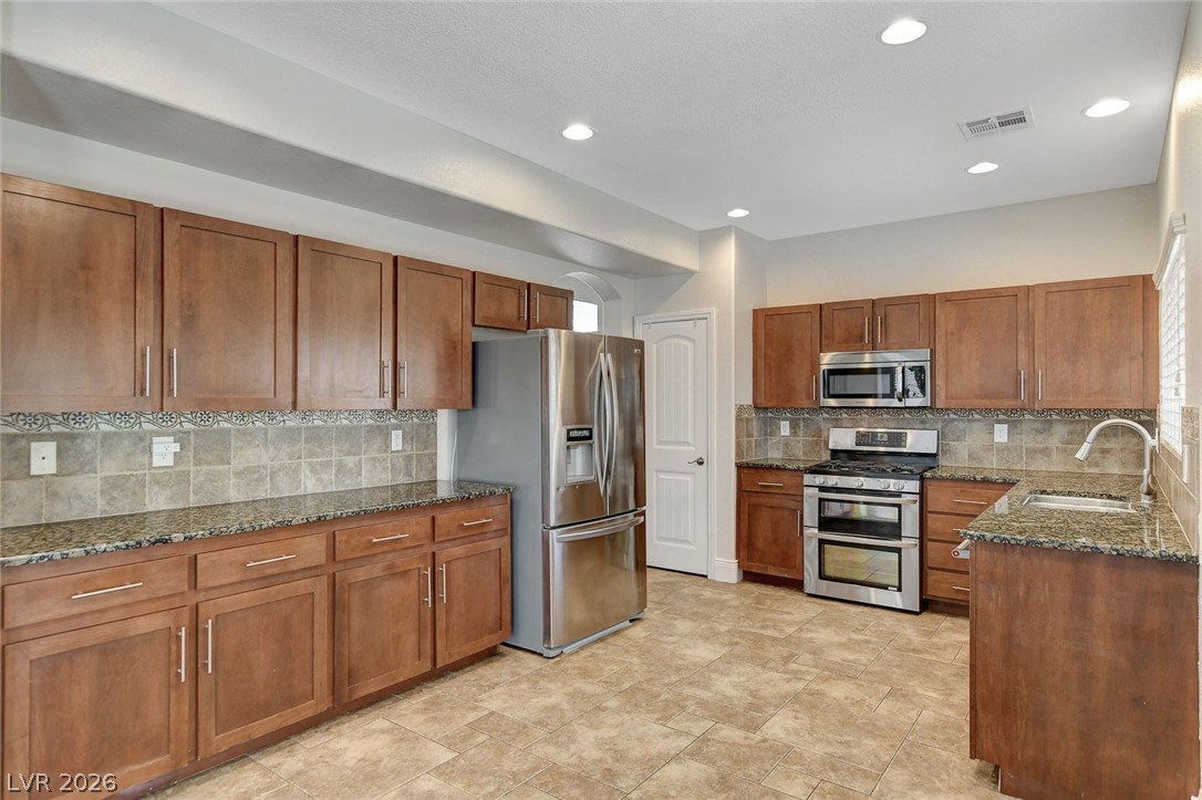 191 Verde Ridge Court Henderson, NV 89012 - Photo 13 of 36 Kitchen featuring stainless steel appliances, a sink, brown cabinetry, dark stone countertops, and recessed lighting