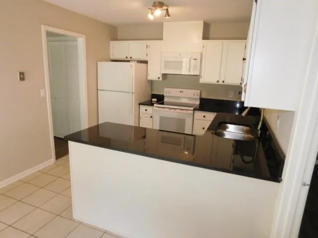 a kitchen with granite countertop a refrigerator a stove a sink and white cabinets